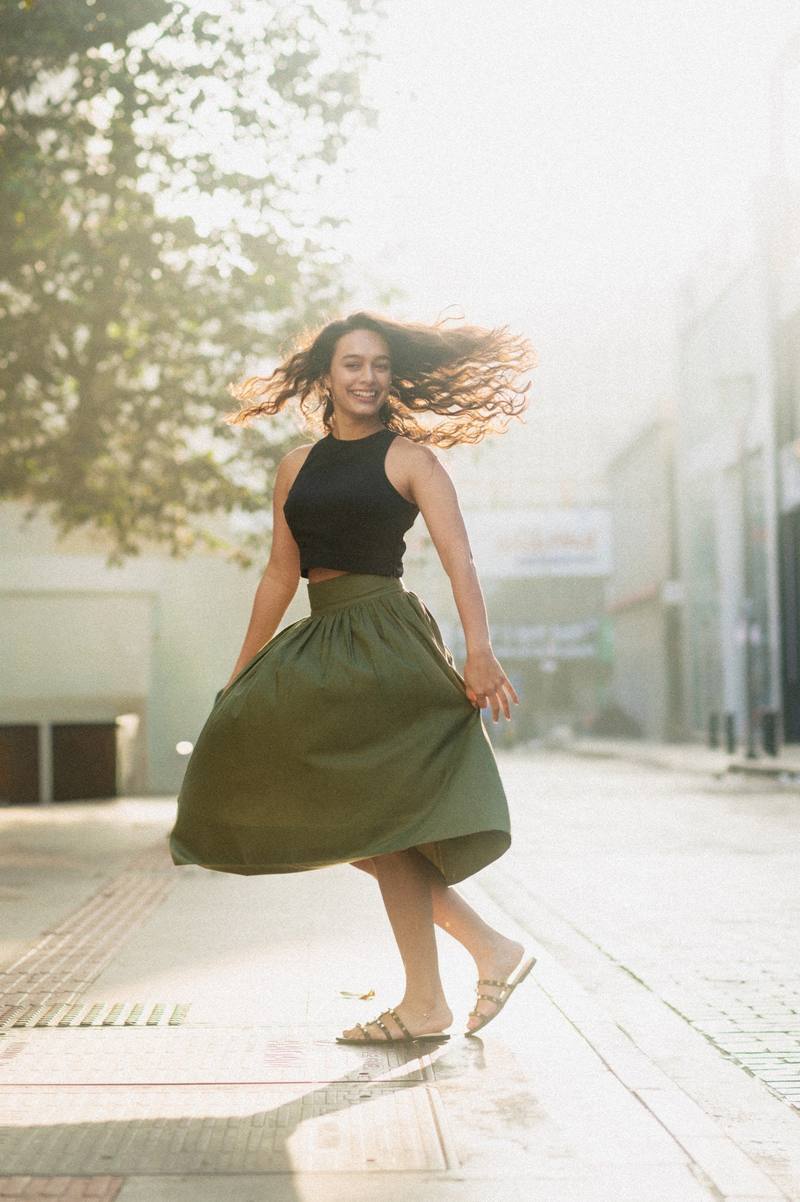 A woman twirling in an olive skirt on a sunlit street