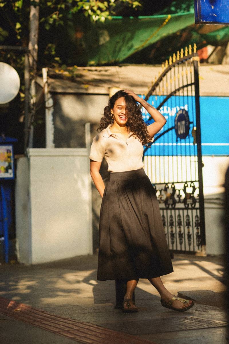 A woman in a black skirt and cream top by a gate